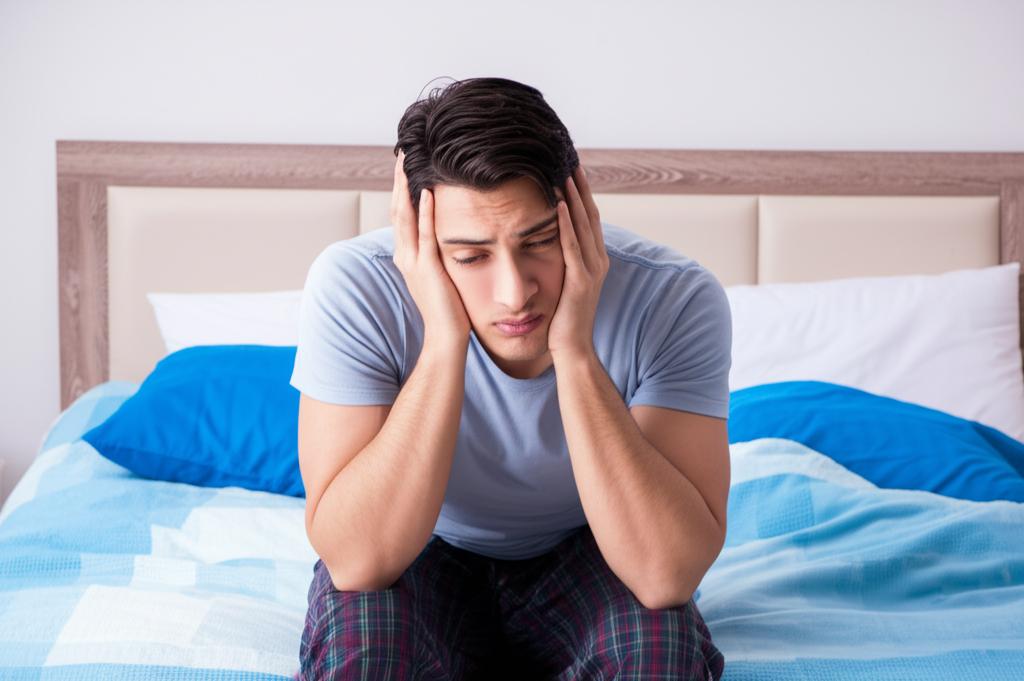 Man looking frustrated and stressed, sitting on a bed with a worried expression, symbolizing relationship problems and performance anxiety.